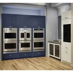 a kitchen with blue cabinets and stainless steel ovens in the center, along with a wood floor