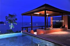 an outdoor gazebo next to a swimming pool at night with the ocean in the background