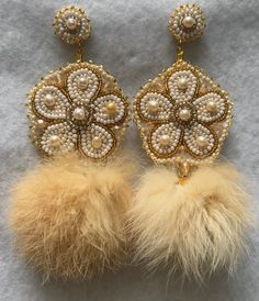 two pairs of earrings with pearls and feathers on top of a gray surface, one is gold