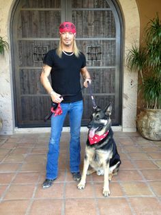 a man standing next to a black and brown dog wearing a bandana on top of it's head