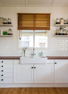 a kitchen with white cabinets and wooden counter tops, open shelving above the sink