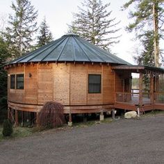 a round wooden building sitting on the side of a road next to some pine trees