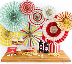 an assortment of colorful paper fans and snacks on a wooden table with popcorn, soda