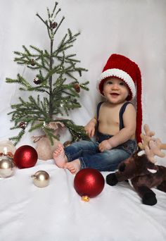 a baby wearing a santa hat sitting next to christmas ornaments and a small fir tree