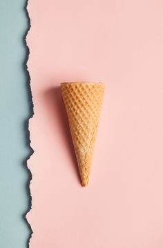 an ice cream cone sitting on top of a pink and blue surface next to a torn piece of paper