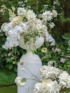 a white vase filled with flowers sitting on top of a cement pillar in front of trees