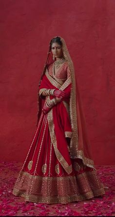 a woman in a red and gold bridal gown posing for the camera with her hands on her hips