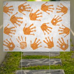 an orange and white handprinted sign in front of a green grass covered yard