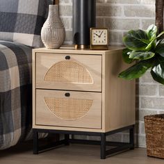 a nightstand with a clock on it next to a bed and a plant in a vase