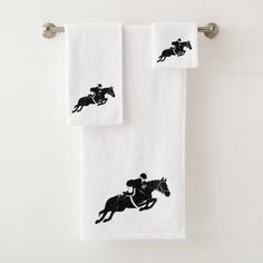 two white towels with horse and jockey silhouettes on them, hanging from the wall