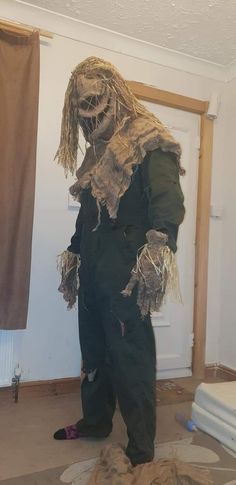 a man dressed as a zombie standing in front of a door with hay on the floor