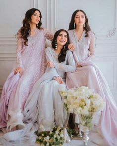 three women sitting next to each other on a white table with flowers in front of them