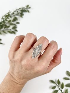 a woman's hand with a diamond ring on top of her finger, next to a plant