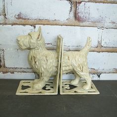 two white dog bookends sitting next to each other on a wooden table with brick wall in the background