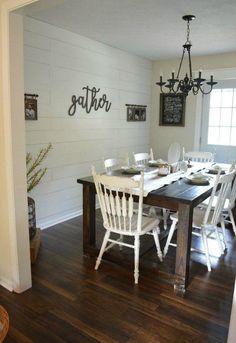 a dining room table with white chairs and a black sign on the wall above it