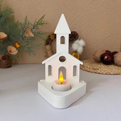 a small white church candle holder with a lit candle in front of it on a table