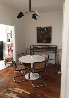 a white table and chairs in a room with wood flooring next to a painting on the wall