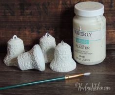 three white ceramic bells sitting next to a paintbrush on top of a wooden table