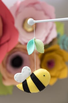 a yellow and black stuffed animal hanging from a string with flowers in the back ground