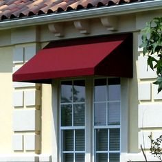 a black awning on the side of a house next to a tree and bushes