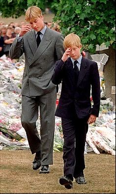 two young boys in suits walking next to each other with people watching them from behind