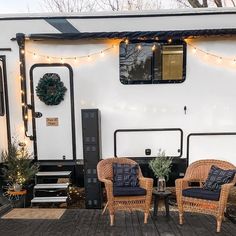 two wicker chairs sitting on top of a wooden deck next to a white trailer