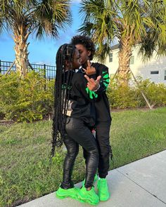 two women standing next to each other in front of palm trees and green shoes on the sidewalk