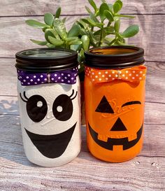 two painted mason jars with faces and pumpkins on them sitting next to each other