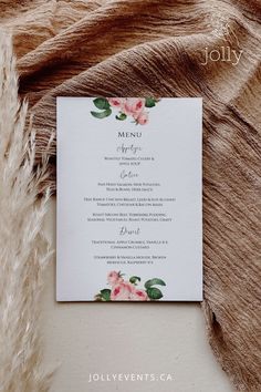 a menu card with pink flowers and greenery on it, next to a furnishing