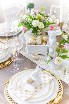 the table is set for easter dinner with white and pink flowers in vases, gold rimmed plates, and bunny figurines