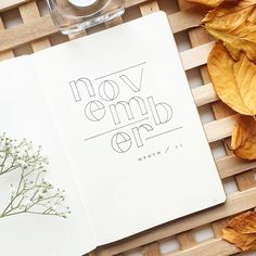 an open notebook with the words november on it next to a glass of water and dried leaves