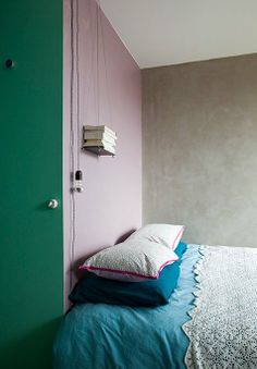 a small bed with pillows and blankets in a room that is painted pink and green