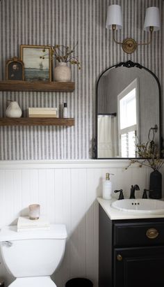 a white toilet sitting next to a sink in a bathroom under a mirror above a wooden shelf