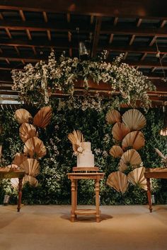 a table topped with a cake and umbrellas next to a wall covered in greenery