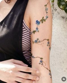 a woman's arm with blue flowers on it and green leaves around the arm