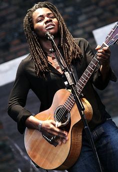 a woman with dreadlocks holding a guitar and singing into a microphone on stage