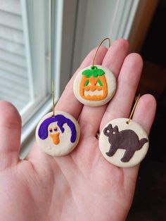 three handmade halloween ornaments are shown in front of a window, and one is holding an animal