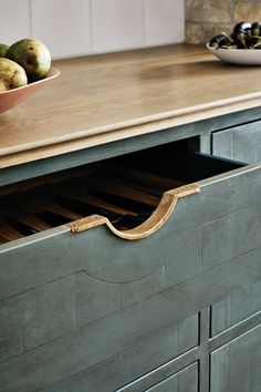 a wooden counter top with drawers and fruit in a bowl on the table next to it