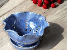 a blue bowl sitting on top of a wooden table next to some strawberries and raspberries