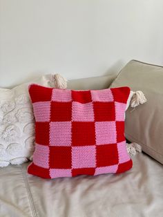 a red and white crocheted pillow sitting on top of a couch next to pillows