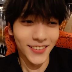 a young man smiling at the camera while wearing a black shirt and orange chair behind him