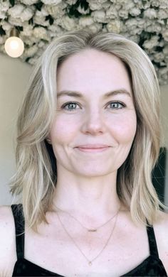 a woman with blonde hair and blue eyes smiling at the camera, wearing a black top