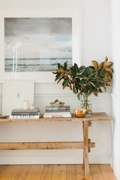 a wooden table topped with books next to a vase filled with flowers on top of a hard wood floor