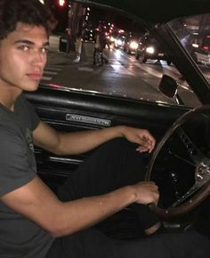 a young man sitting in the driver's seat of a car on a city street at night