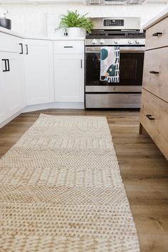 a kitchen with white cabinets and an area rug on the floor in front of the stove