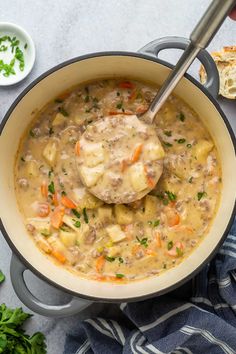 a pot filled with soup and meatballs on top of a blue towel next to bread