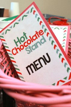 a pink basket filled with food next to a sign that says hot chocolate stand menu