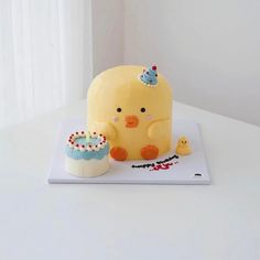 a cake shaped like a bird with a cupcake on it's plate next to a toy duck