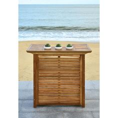 a wooden table sitting on top of a sandy beach next to the ocean with succulents