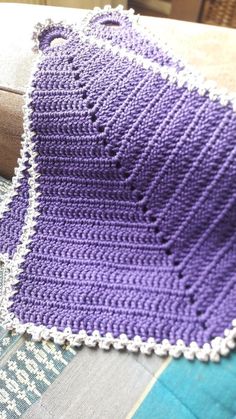 a purple crocheted blanket sitting on top of a blue and white table cloth